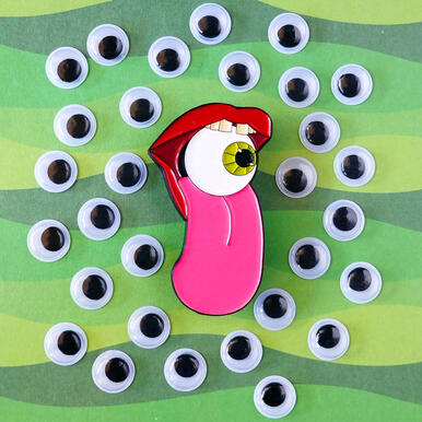 an enamel pin depicting a mouth sticking its tongue out, with an eyeball in it.